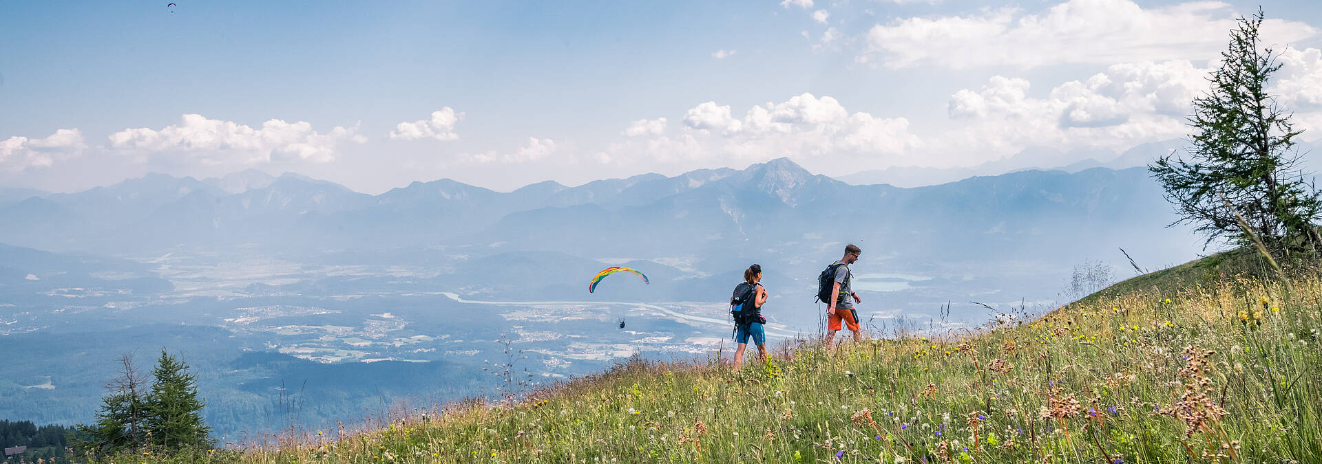 Pärchen beim Wandern auf der Gerlitzen Alpe mit Paragleiter im Hintergrund
