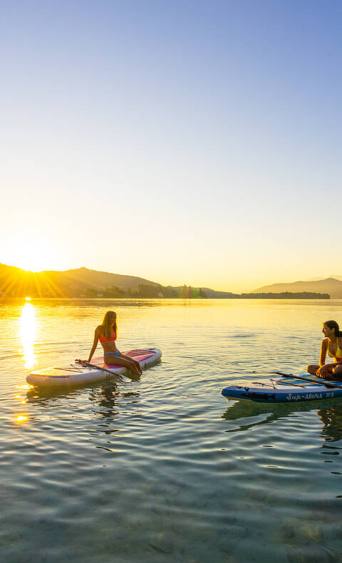 Zwei Damen bei Sonnenuntergang am Woerthersee mit Boot und Paddel